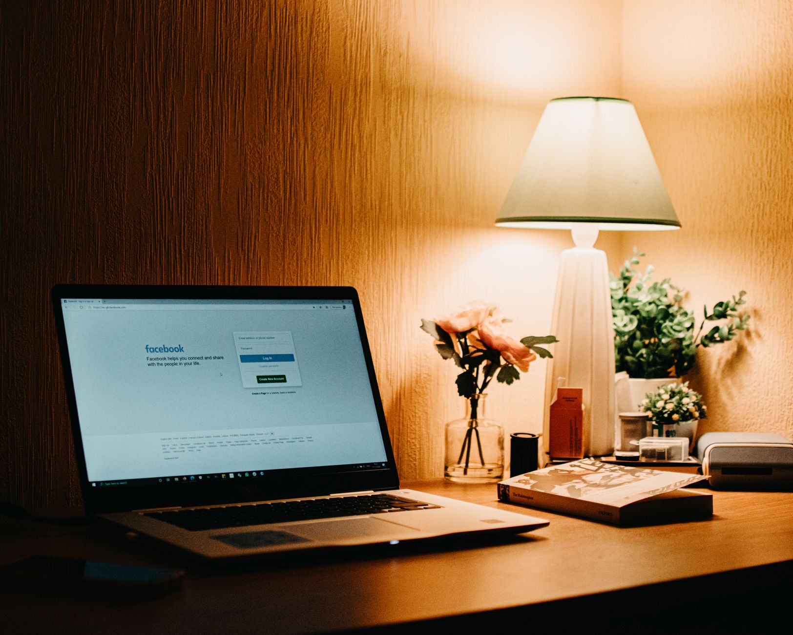 Warmly lit home workspace with a laptop, a lamp and a few personal items on the desk.