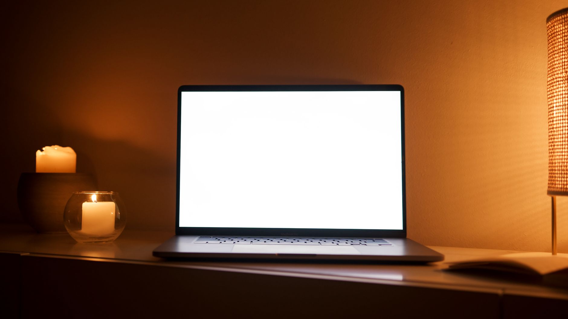 Warm-toned home workspace with a laptop and lit candles beside it.